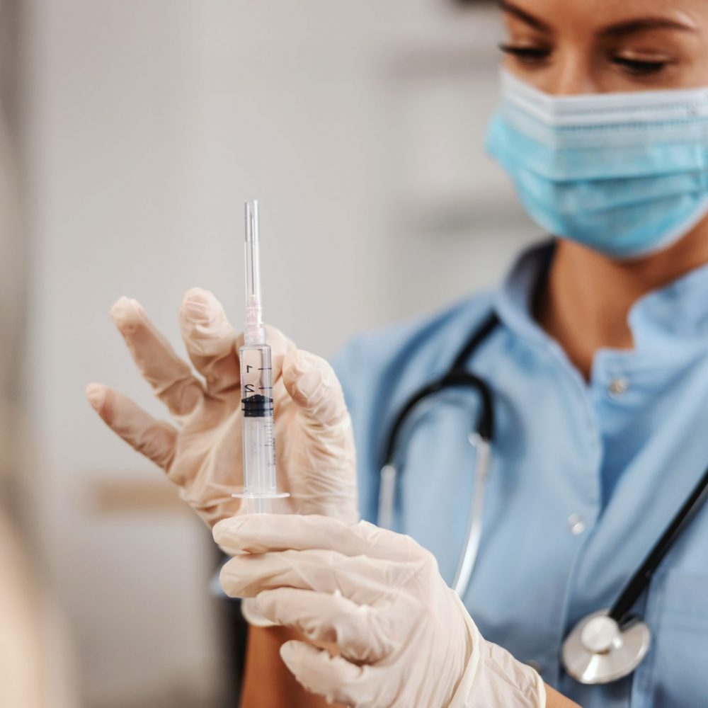 Closeup of nurse with face mask on preparing injection.